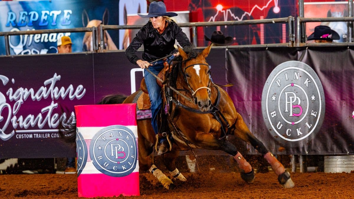 Alona James turns a barrel with two hands on the reins on her dark mare