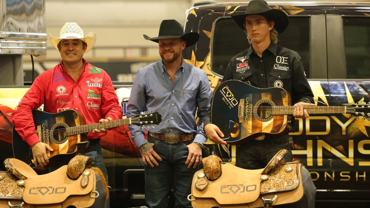 Kaleb Driggers, Cody Johnson and Nicky Northcott behind two COJO trophy saddles, Driggers and Northcott holding guitars.