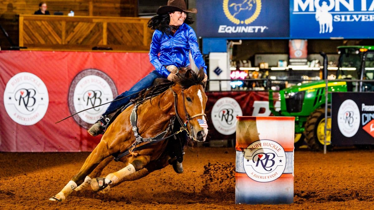 heidi Gunderson sits on a horse turning a barrel in a blue shirt