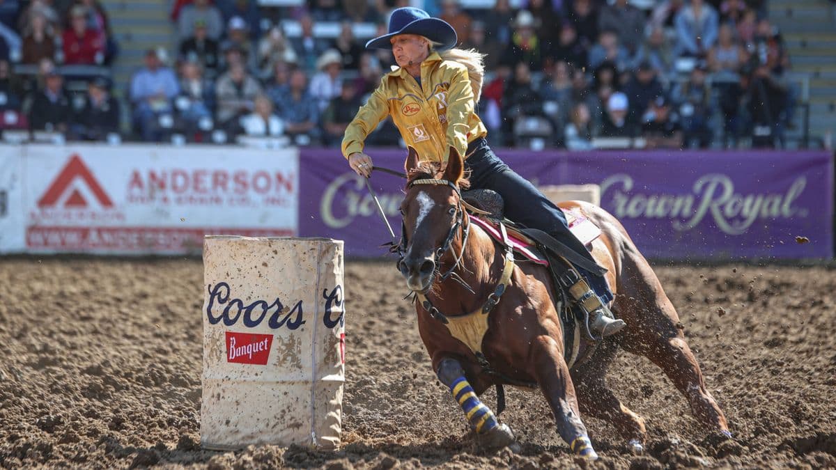 Summer Kosel turns a barrel in a yellow shirt in the mud on her horse