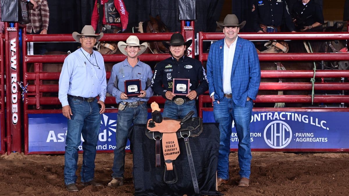 J.C. Yeahquo and Kelby Frizzell hold award buckles behind a trophy saddle at the Texas Circuit Finals in Waco, Texas.