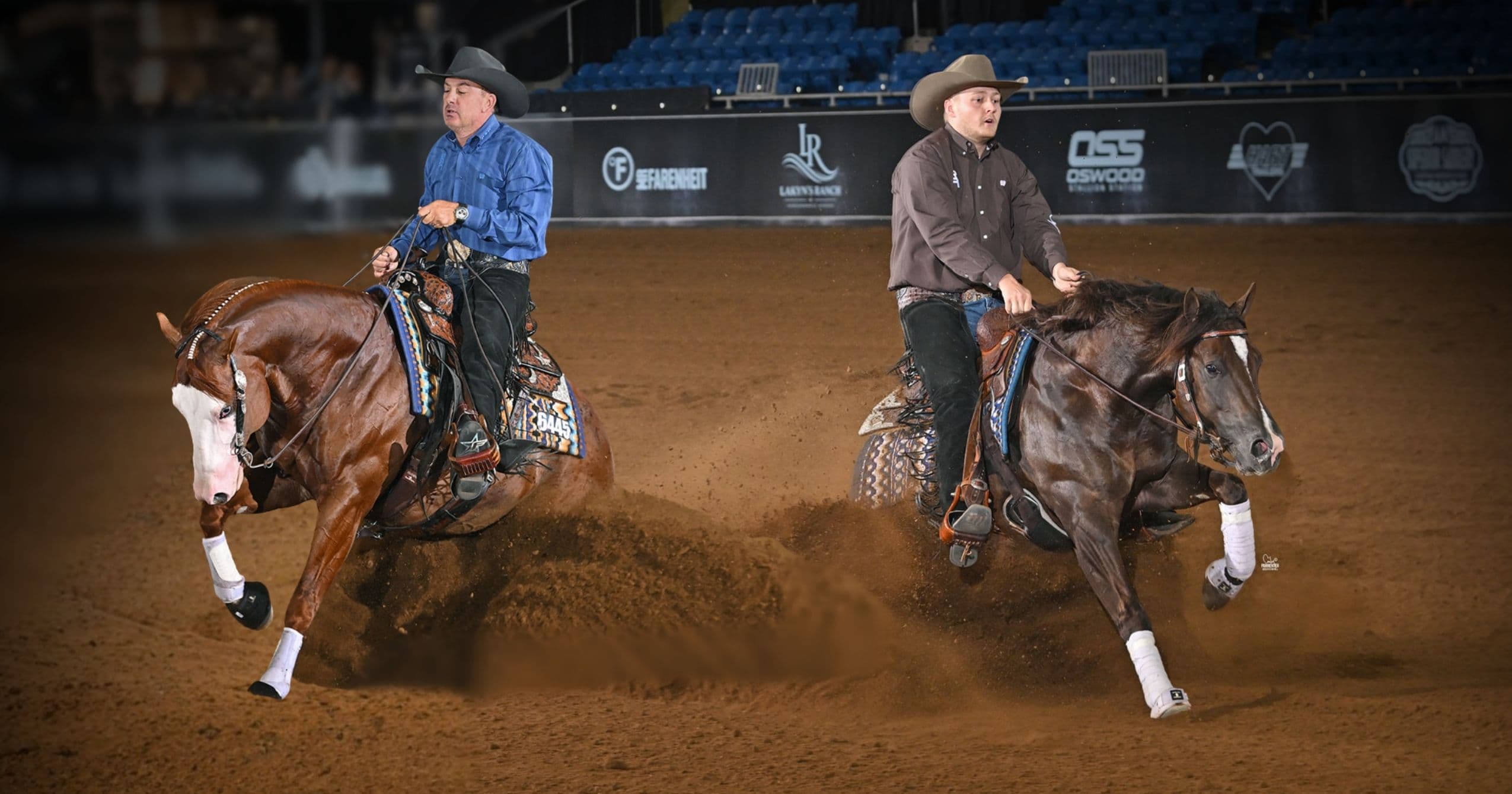 Two reining riders in cowboy hats slide their sorrel horses to a stop in opposite directions, kicking up arena dirt