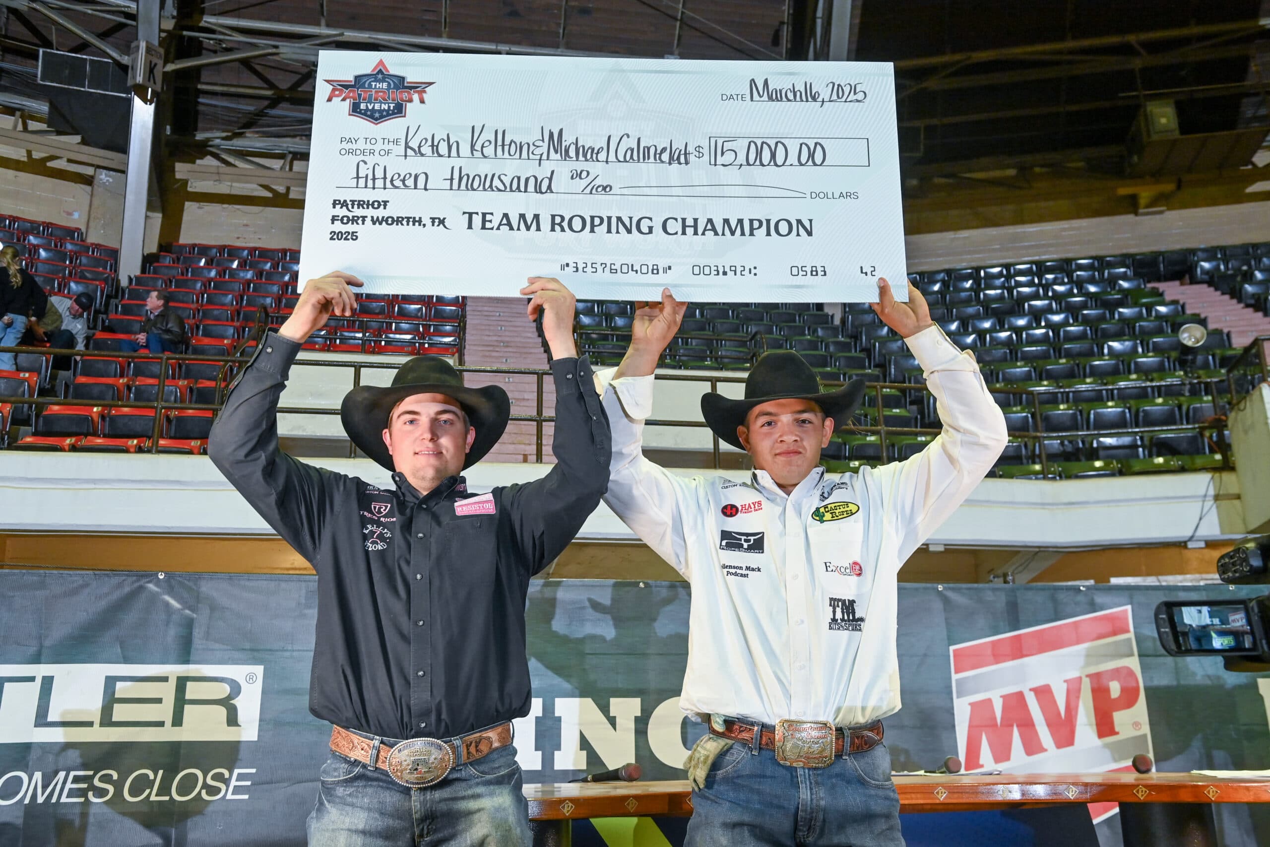 Team ropers hold oversized check for $115,000 at 2025 Patriot Fort Worth event, wearing cowboy hats and championship buckles