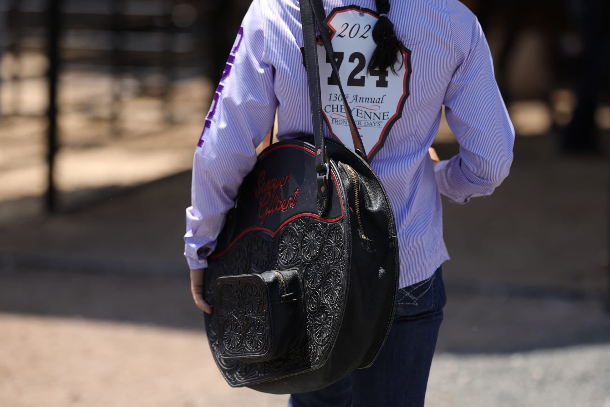 Contestant in a striped shirt wearing back number 724 at Cheyenne Frontier Days, carrying a tooled black rope bag