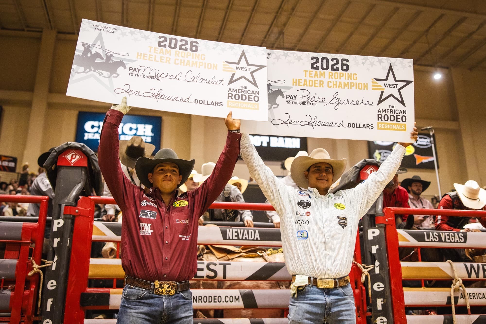Two team ropers celebrate holding the 2026 American Rodeo Regionals Team Roping Header Champion checks for ten thousand dollars each at Las Vegas rodeo