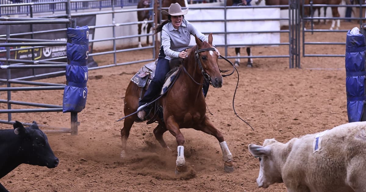 Smiling cowgirl in a straw hat rides a sorrel horse hard through the arena dirt, working cattle in a ranch sorting pen