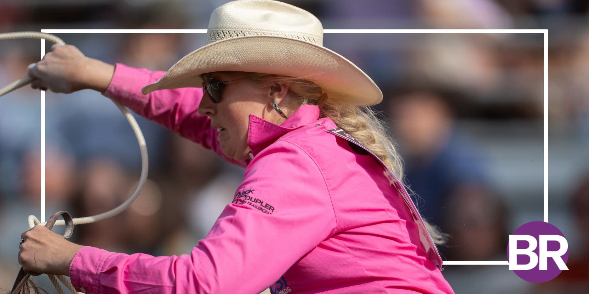 Breakaway roper in a pink shirt and straw cowboy hat swings her loop overhead during a rodeo run