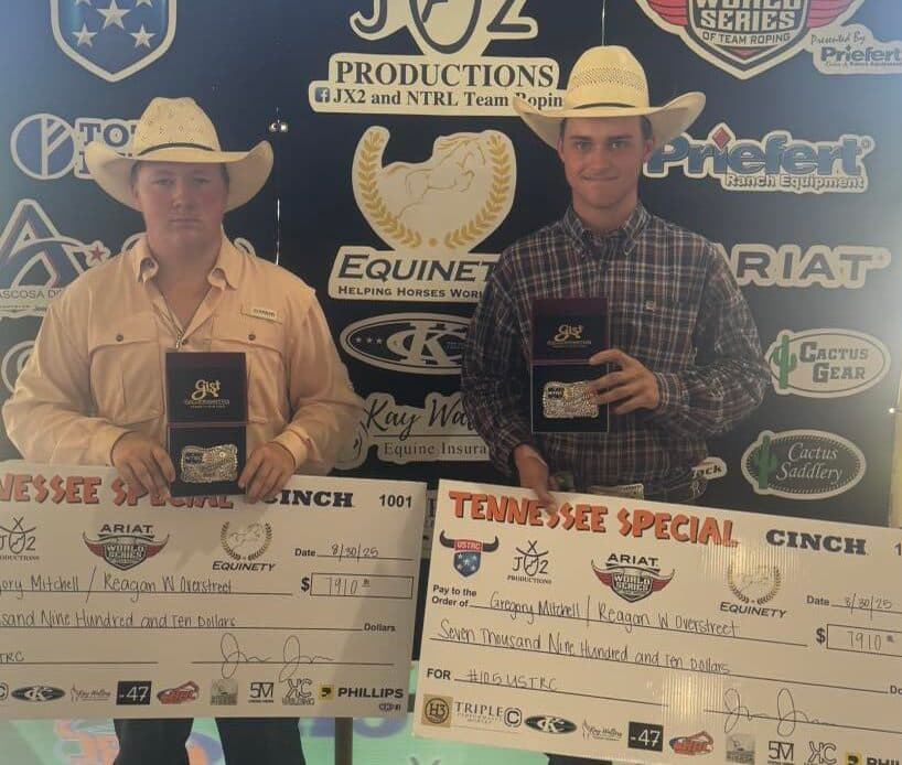 Two team ropers in cowboy hats hold championship buckles and oversized Tennessee Special winner's checks at a sponsor backdrop