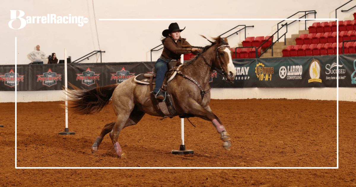 Young rider in a black cowboy hat leans into a turn around a pole on a dun roan horse in an indoor arena