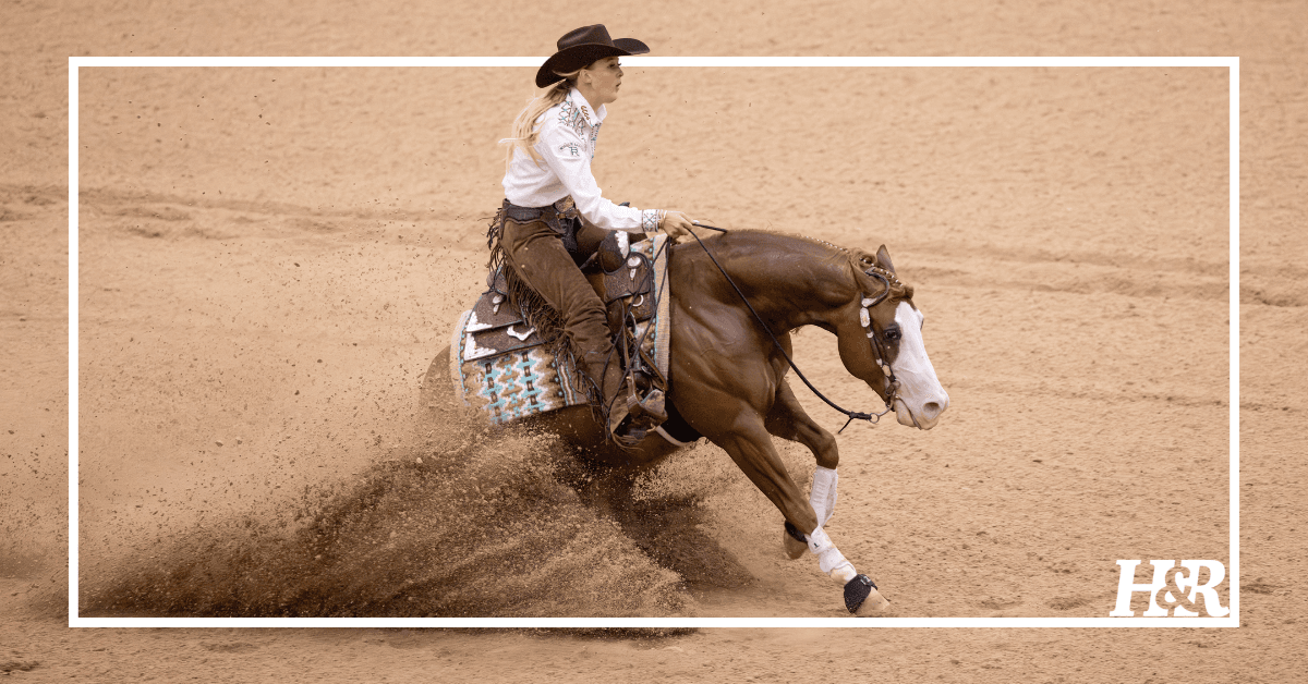 Reining rider in black cowboy hat and chaps executing a sliding stop on a sorrel horse, dirt spraying behind