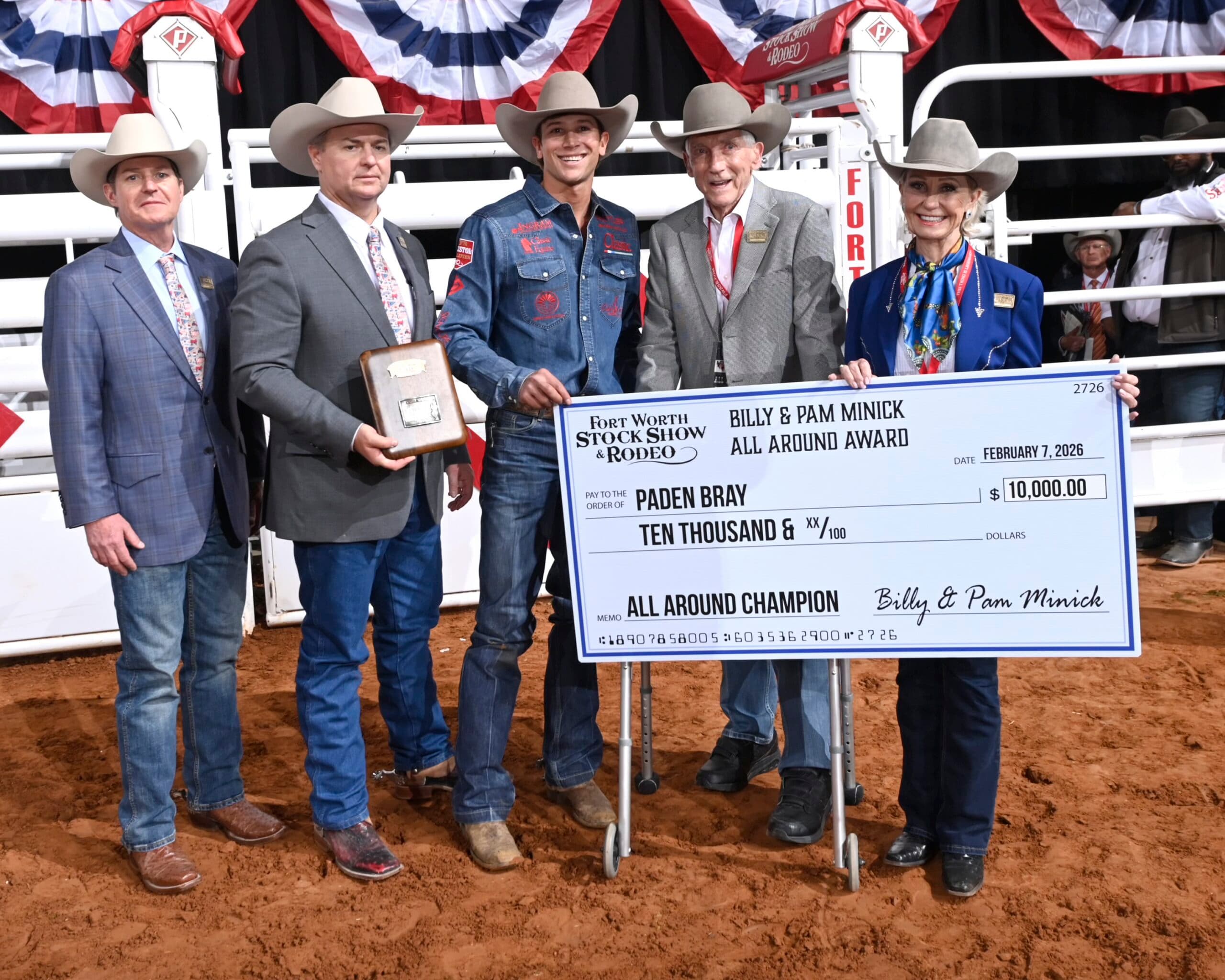 Paden Bray holds a $10,000 check after winning the Billy & Pam Minick All Around Award at the Fort Worth Stock Show & Rodeo, flanked by officials at the arena