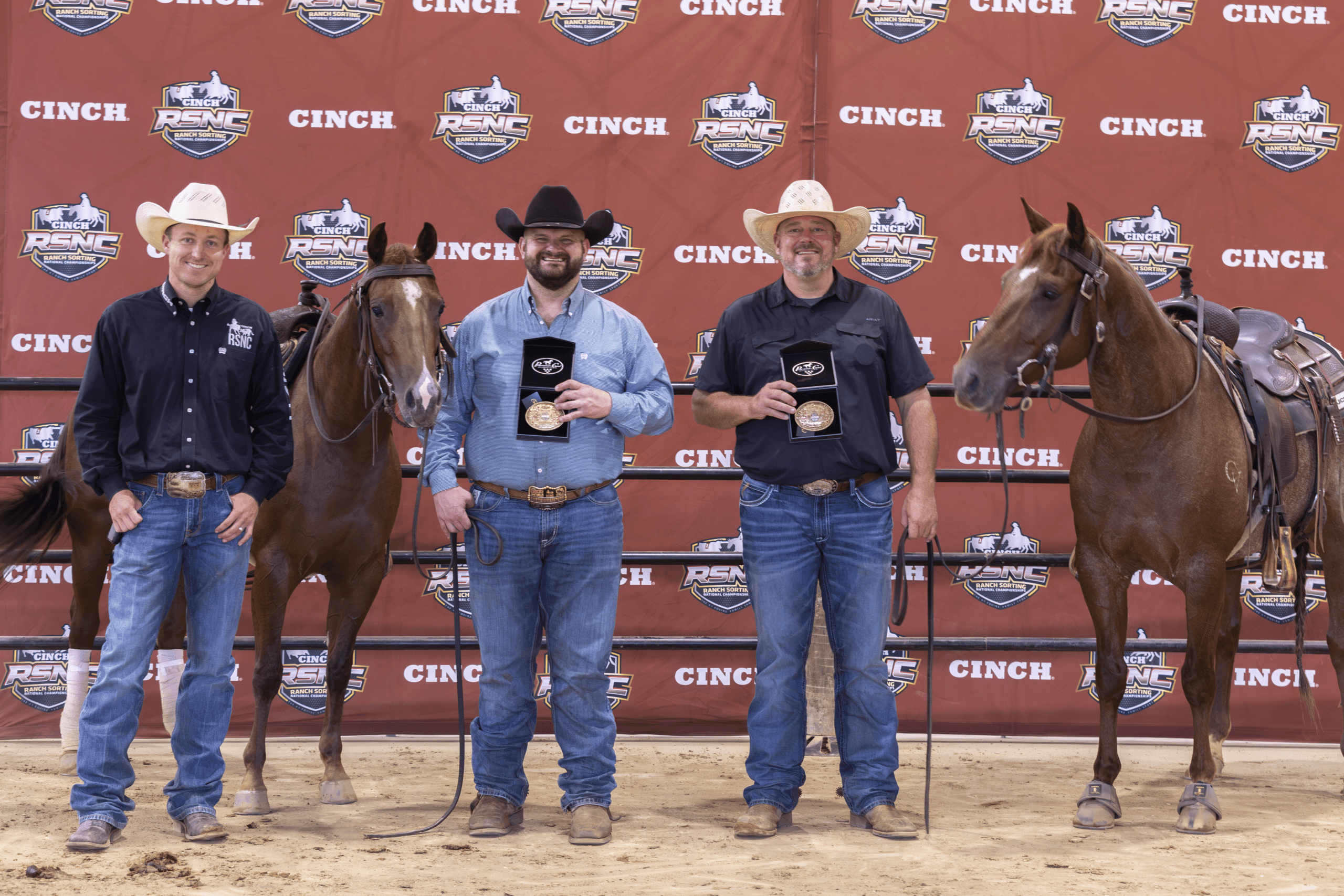 Five cowboys and two horses stand at a CINCH-branded backdrop during an awards presentation at a rodeo event