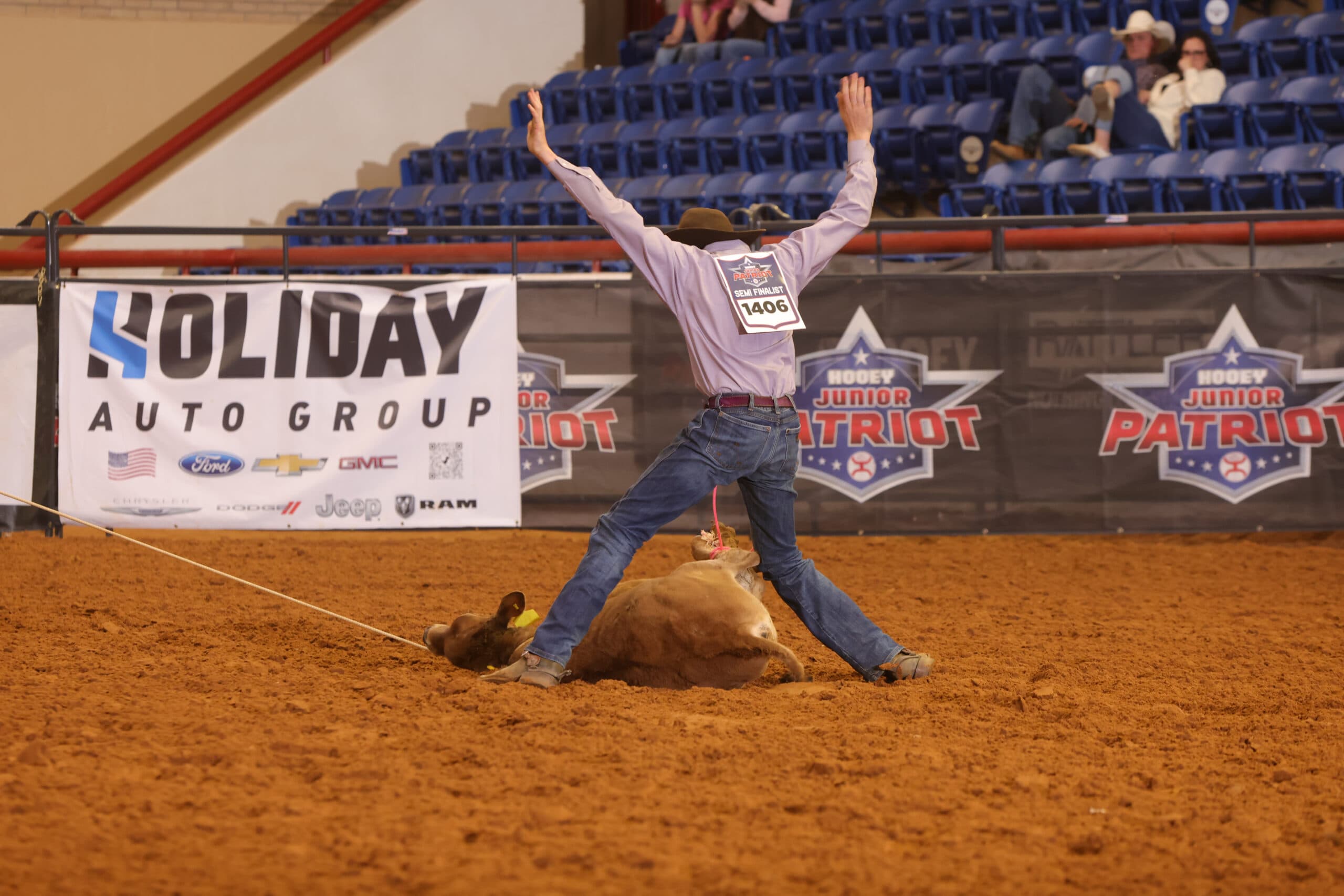 Tie-down roper wearing number 1406 throws both hands in the air after tying his calf in the arena dirt