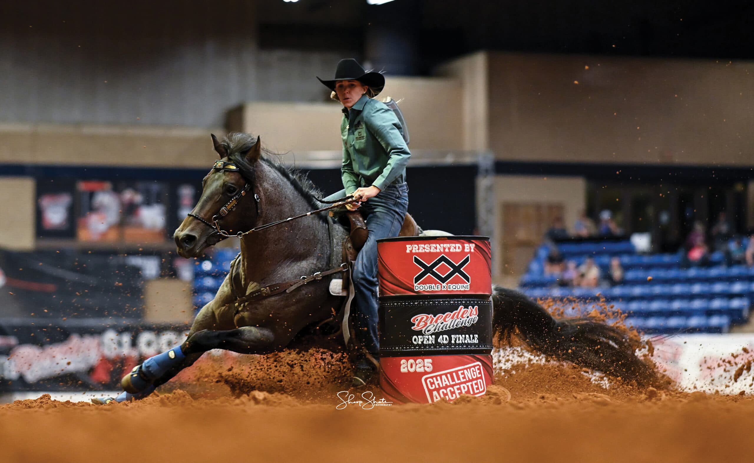 Barrel racer on dark horse executing a tight turn around a barrel at an indoor rodeo arena during the Wrangler National Finals Rodeo Open 4D Finals