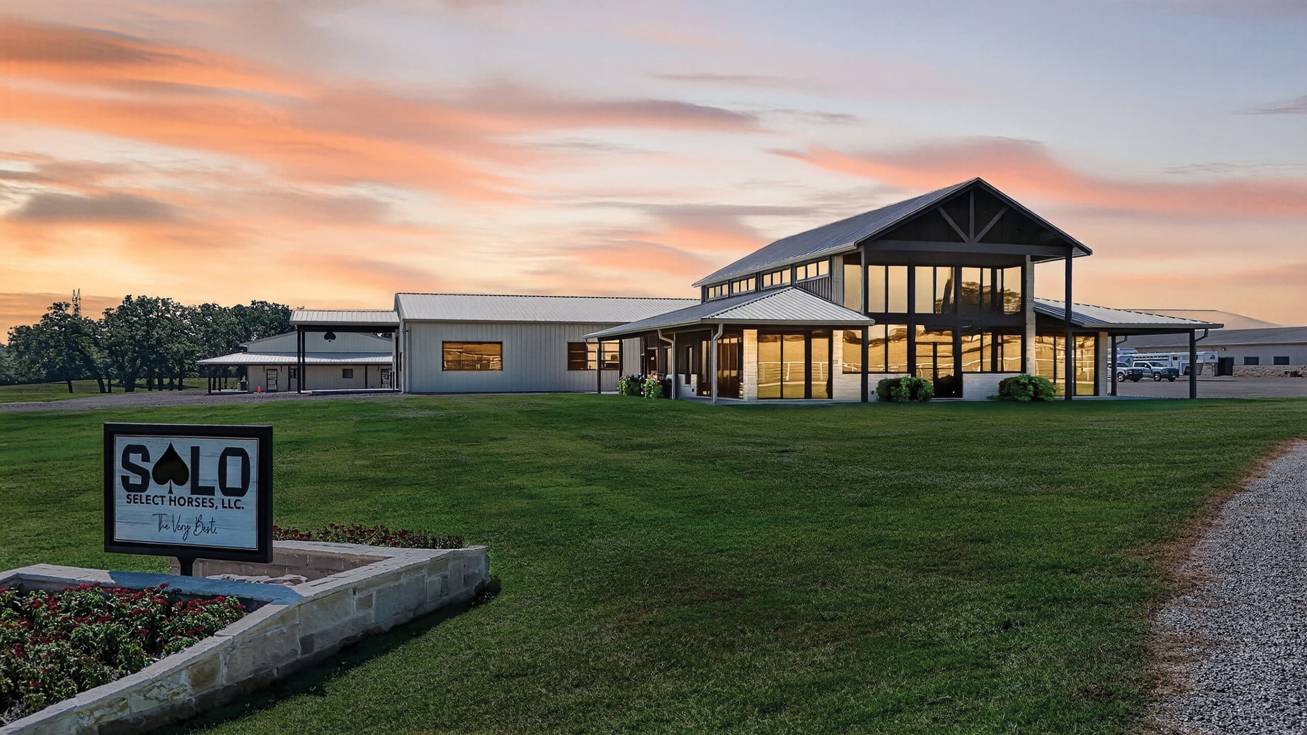 SOLO Select Horses facility entrance at dusk, with modern barn and arena buildings illuminated against a sunset sky