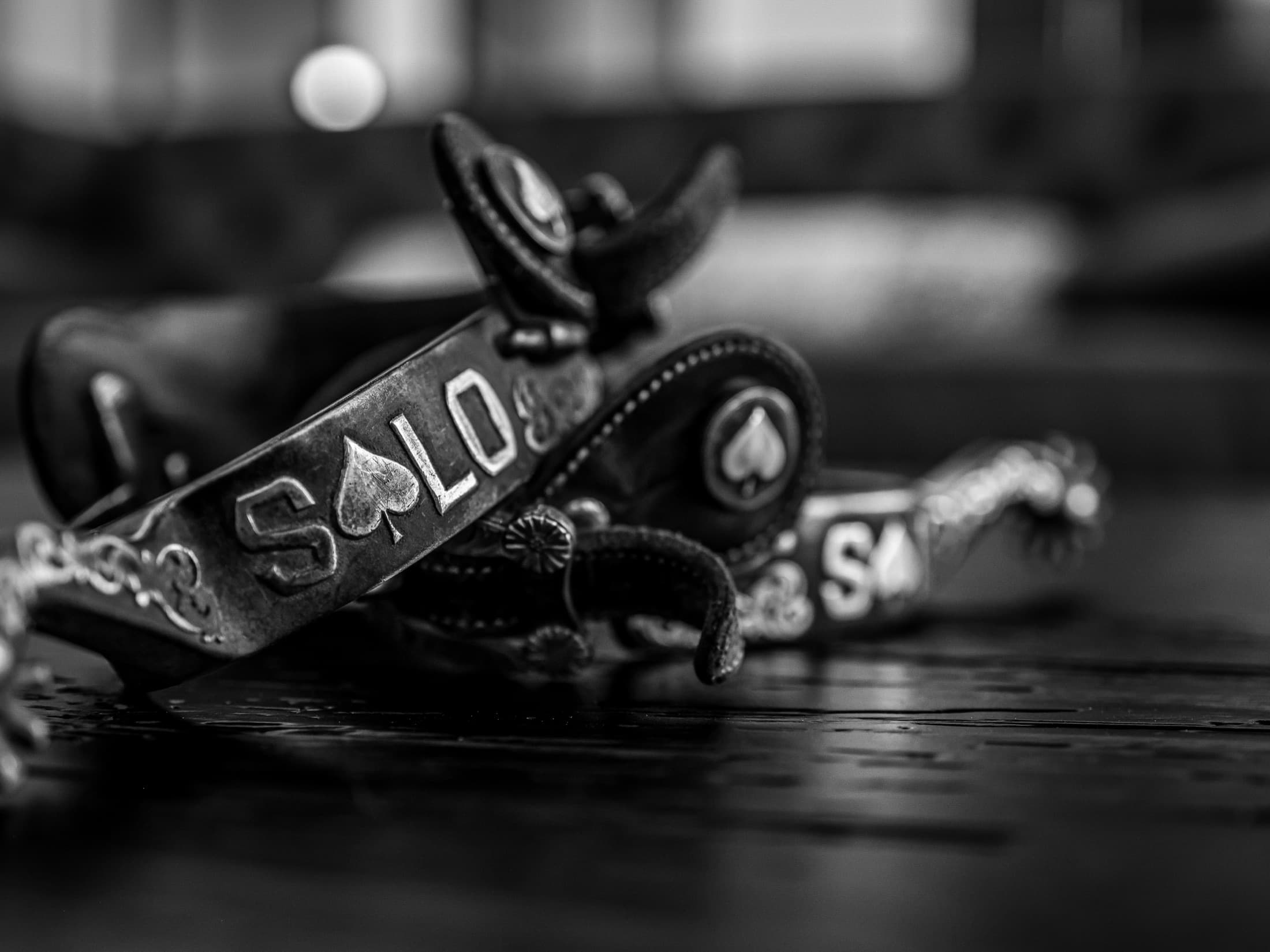 Ornate leather rodeo equipment with "SALTO" text and spade suit emblem lies on dark wooden surface with a ball visible above