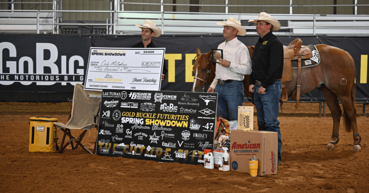 Three men in cowboy hats stand with an oversized $10,000 Spring Showdown check, sponsor banner, prizes and a saddled sorrel horse in an arena