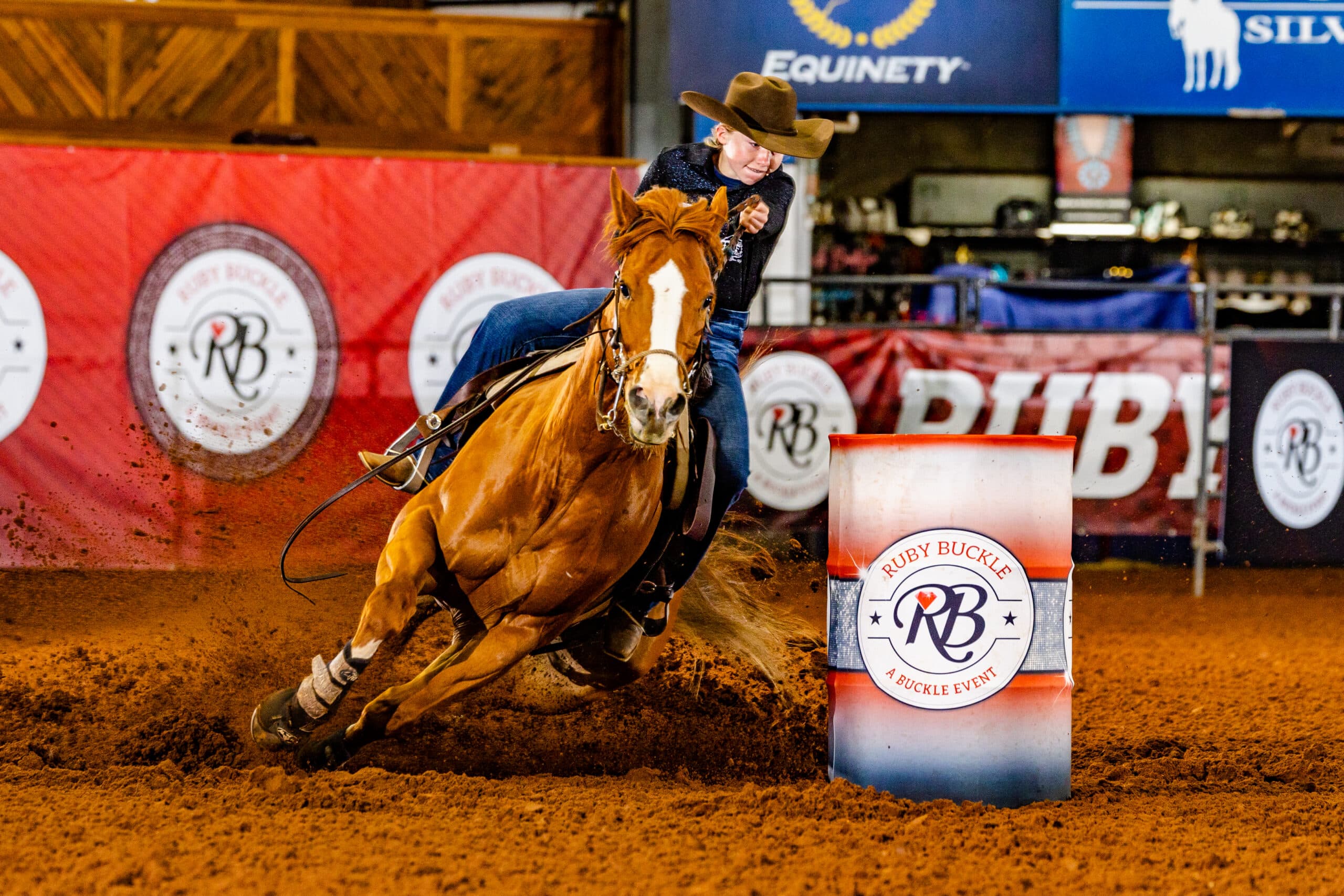 Macey Moore in a brown hat and black shirt turns a barrel on her red horse