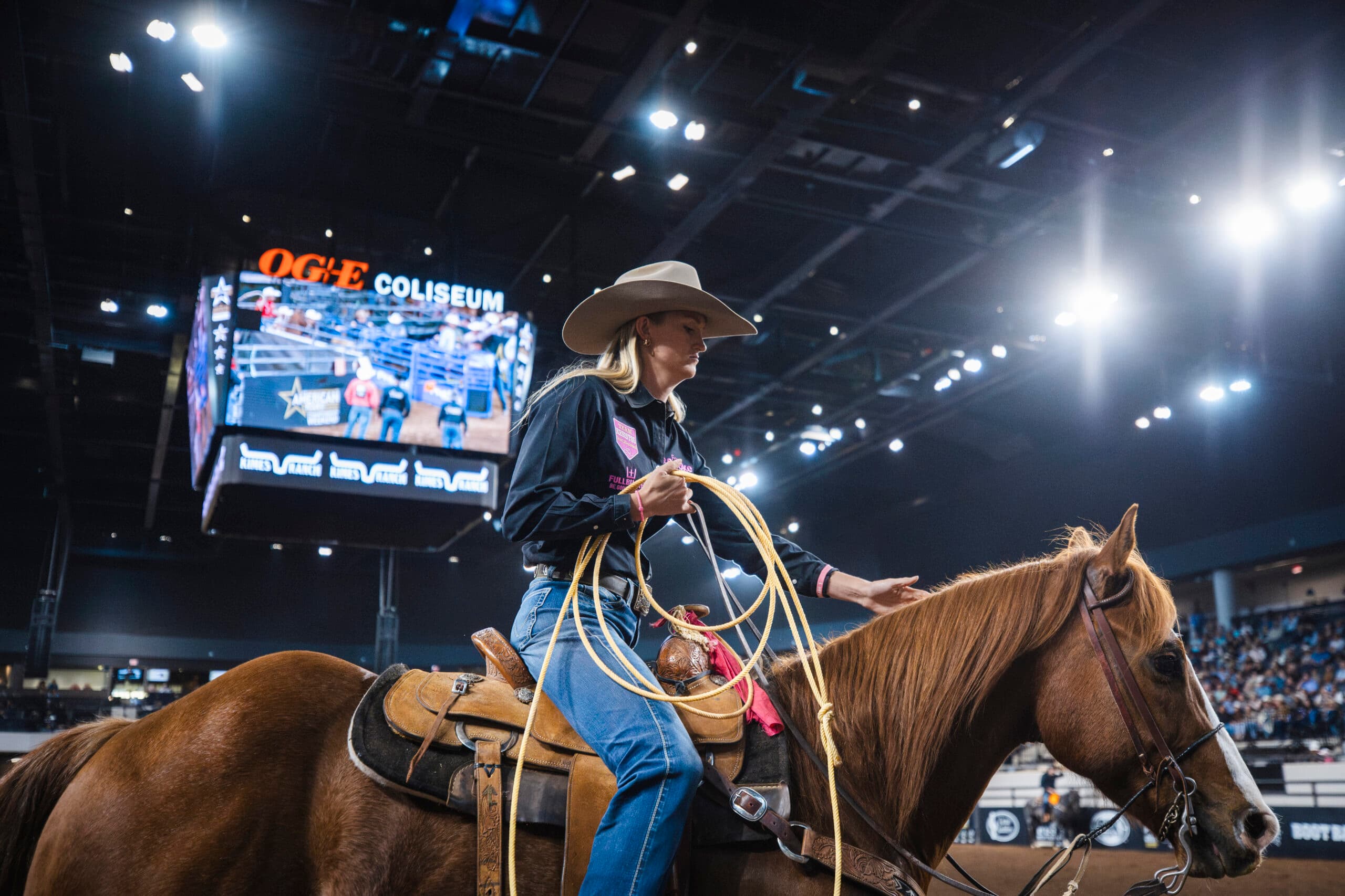 Breakaway roper in a cowboy hat coils her rope and pats her sorrel horse's neck inside the OG&E Coliseum arena