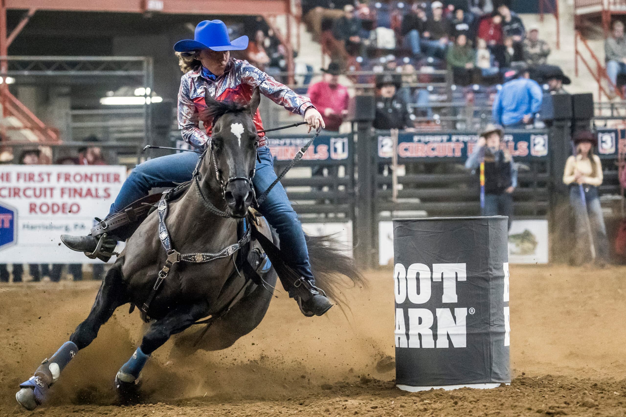 Willie Horzepa turns a barrel in a blue hat on her black horse Diva